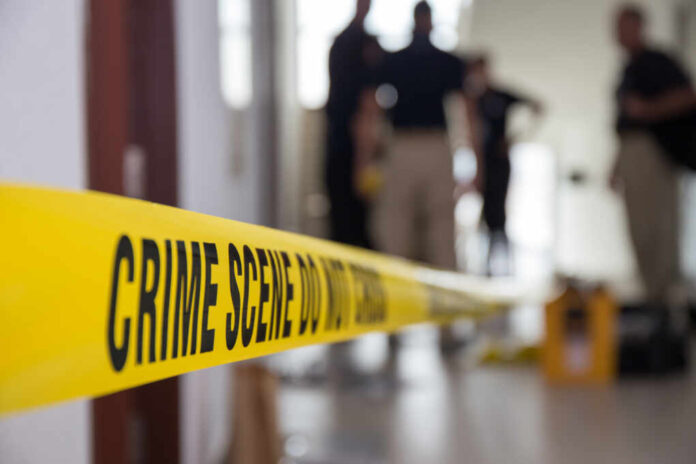 Crime,Scene,Tape,In,Building,With,Blurred,Forensic,Team,Background